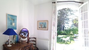 Een kamer met uitzicht op een tuin, een houten dressoir, een spiegel en een lamp.