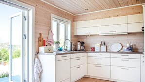 A modern kitchen with white cabinets, a wooden ceiling, and a view of greenery outside. - 3 bedroom awesome home in Skjold (Skjold)
