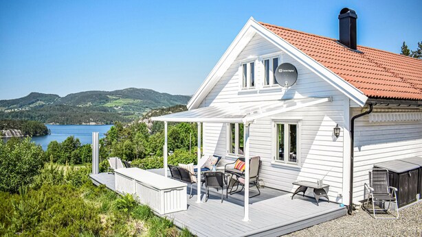 A white house with a red roof, a deck with outdoor furniture, and a view of a lake and hills. - 3 bedroom awesome home in Skjold (Skjold)