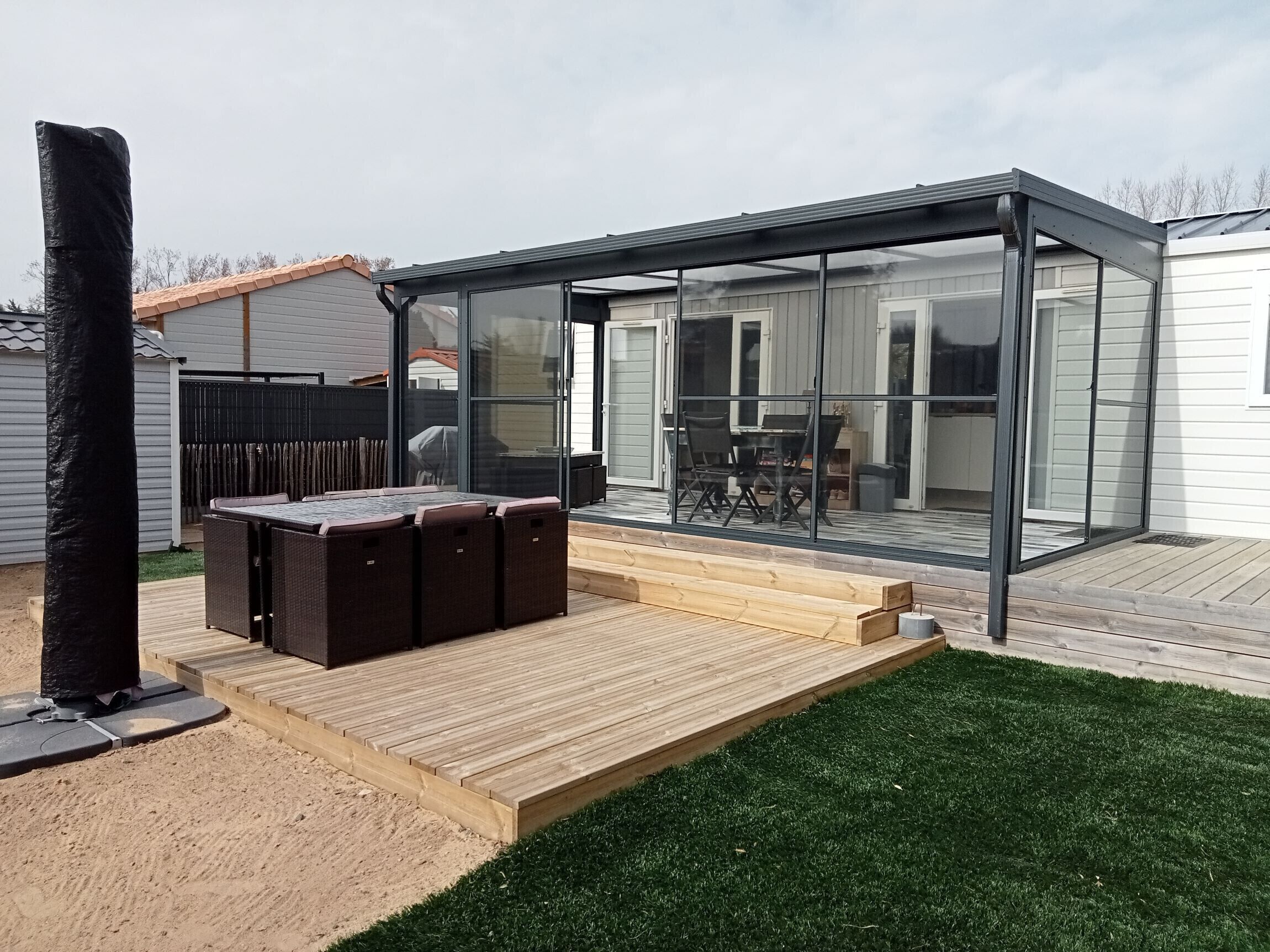 Une terrasse extérieure moderne, dotée d’une véranda en verre, d’une terrasse en bois et d’un espace salon avec une table et des chaises.