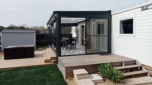 Un patio exterior moderno con cerramiento de vidrio, una pequeña zona ajardinada y una terraza de madera.
