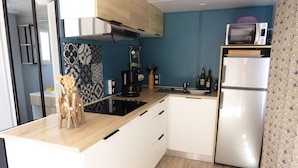 Cocina compacta con armarios blancos, una campana extractora de acero inoxidable, un microondas y un refrigerador.