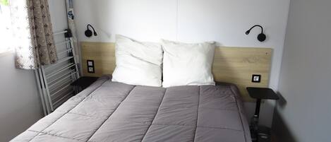 Un lit bien fait, avec une couverture grise, une tête de lit en bois et deux lampes de chevet.
