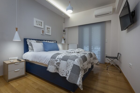 Un dormitorio con cama, mesitas de noche, televisor y ventana con cortinas.