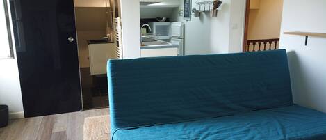 A room with a teal sofa, a small kitchenette, and a bathroom visible through an open door.