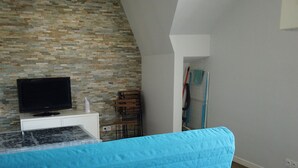 A room with a television on a white cabinet, a patterned table, a blue sofa, and a brick-patterned wall. - 350m from the beach - flat for 4 (Pornichet)
