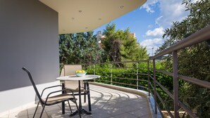 Un balcon avec une table et des chaises, une balustrade et une vue sur la verdure et les bâtiments.