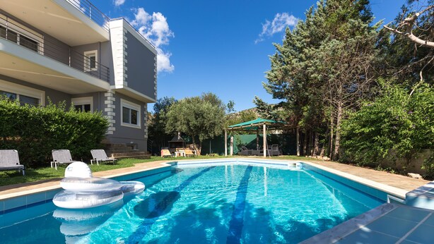 Une piscine avec des bouées gonflables, un espace de repos abrité et un bâtiment doté de balcons.