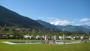 Uma área de piscina com espreguiçadeiras e guarda-sóis, cercada por vegetação exuberante e montanhas ao fundo.