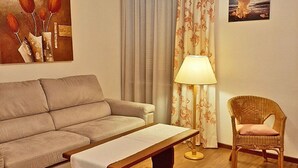 Un salon avec un canapé, un banc, un fauteuil, une lampe et un tableau accroché au mur.