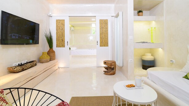 A modern living room with a flat-screen TV, a sofa, a coffee table, and a small wooden stool. - Mykonos 52m² Luxury Apartment Sea side Ornos (Mykonos)