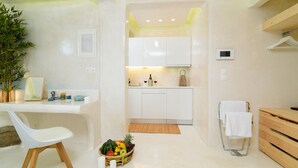 A modern kitchen with white cabinets, a dining area with a white chair, and a fruit basket on the counter. - Mykonos 52m² Luxury Apartment Sea side Ornos (Mykonos)