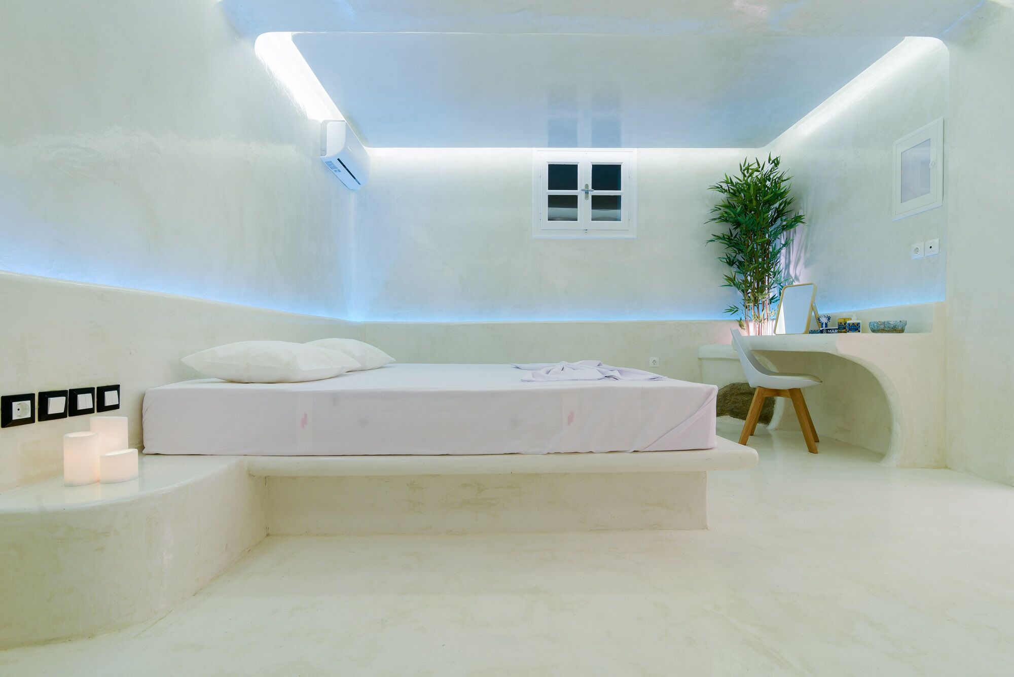 A modern, minimalist bedroom with a bed, bedside table, and a small desk area.