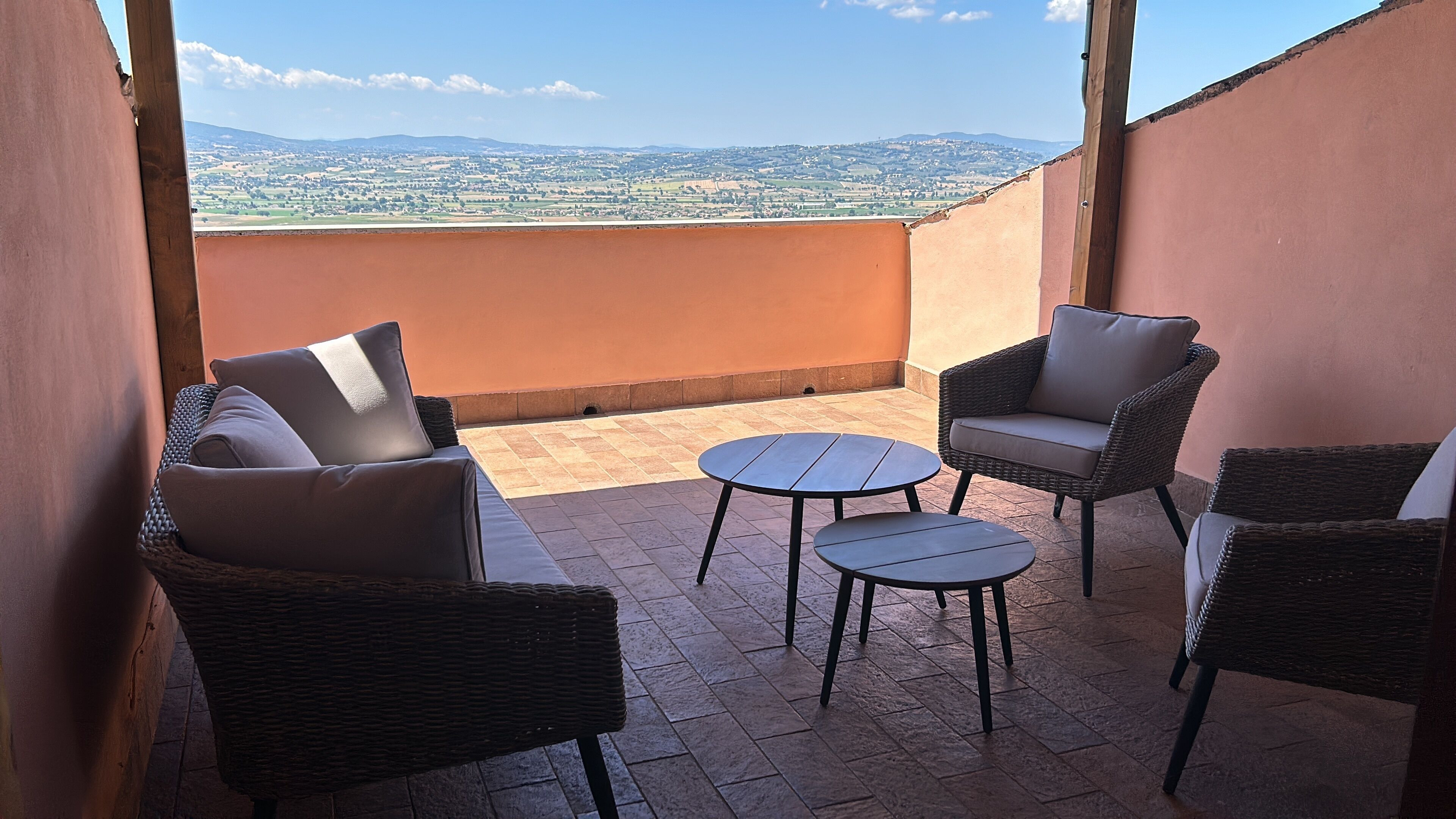 Un balcone con mobili in vimini, un tavolino rotondo e vista su dolci colline.