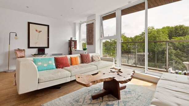 Ein modernes Wohnzimmer mit großem Fenster, einem weißen Sofa, einem Couchtisch und einem Bücherregal.