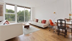 Ein modernes Wohnzimmer mit einem weißen Sofa, einem Esstisch mit Stühlen und großen Fenstern mit Blick auf Grünflächen.
