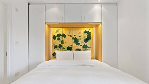 Ein Schlafzimmer mit einem Bett, weißer Bettwäsche, einem Kopfteil mit dekorativer Zierleiste und weißen Schränken oberhalb des Bettes.