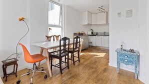 Eine moderne Küche mit weißen Schränken, einem Essbereich mit Holztisch und Stühlen sowie einem blauen Tischchen mit Muster.