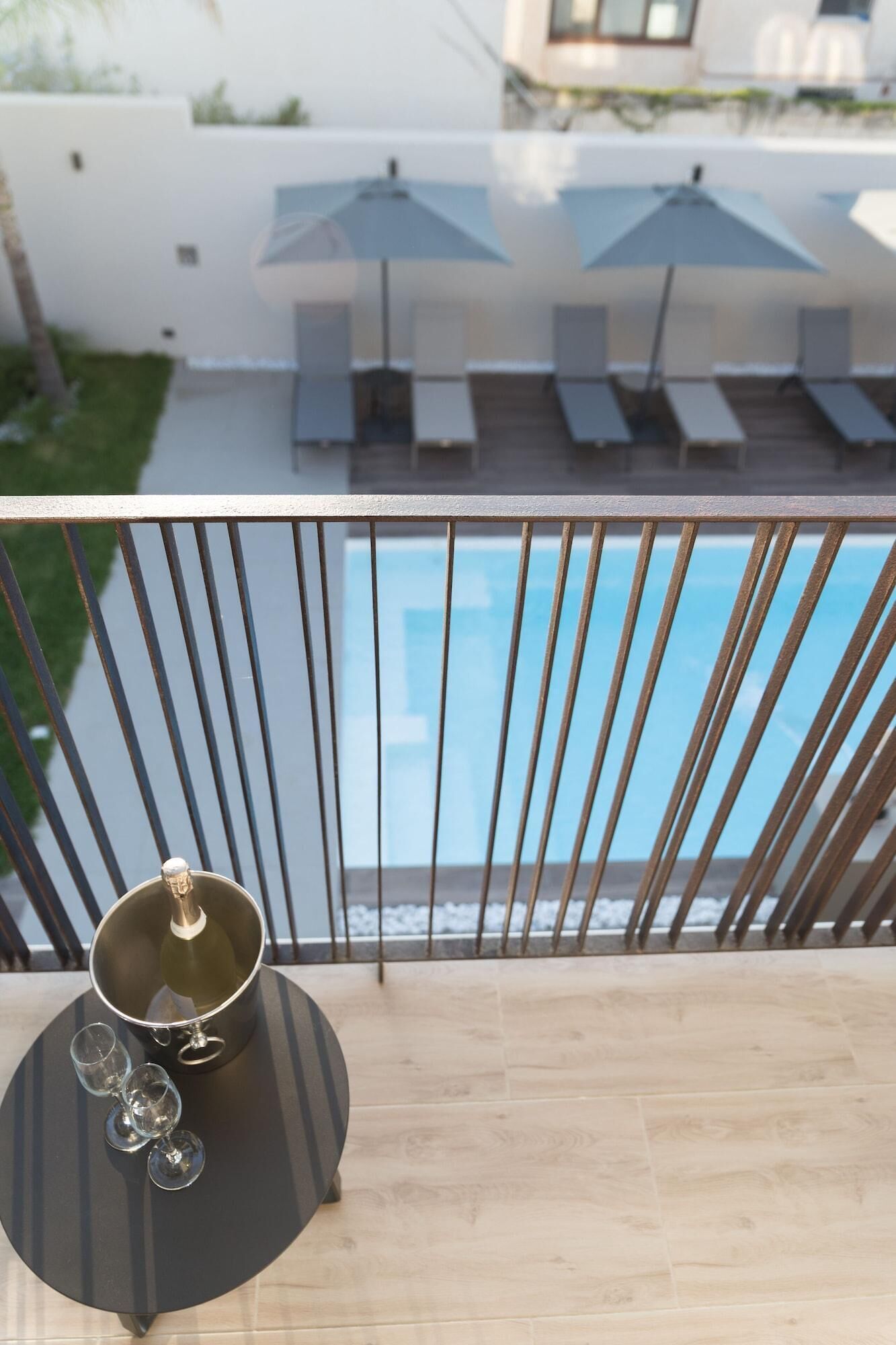 A balcony with a pool, lounge chairs, and a table with a pot and glasses.
