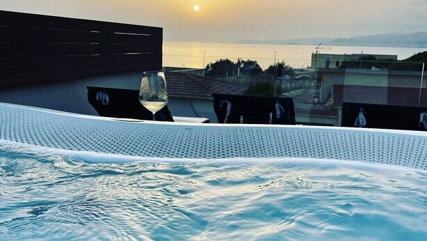 A rooftop pool area with a glass of wine and a glass of water, overlooking a sunset over a body of water. - Giafra Rooms (Agrigento)