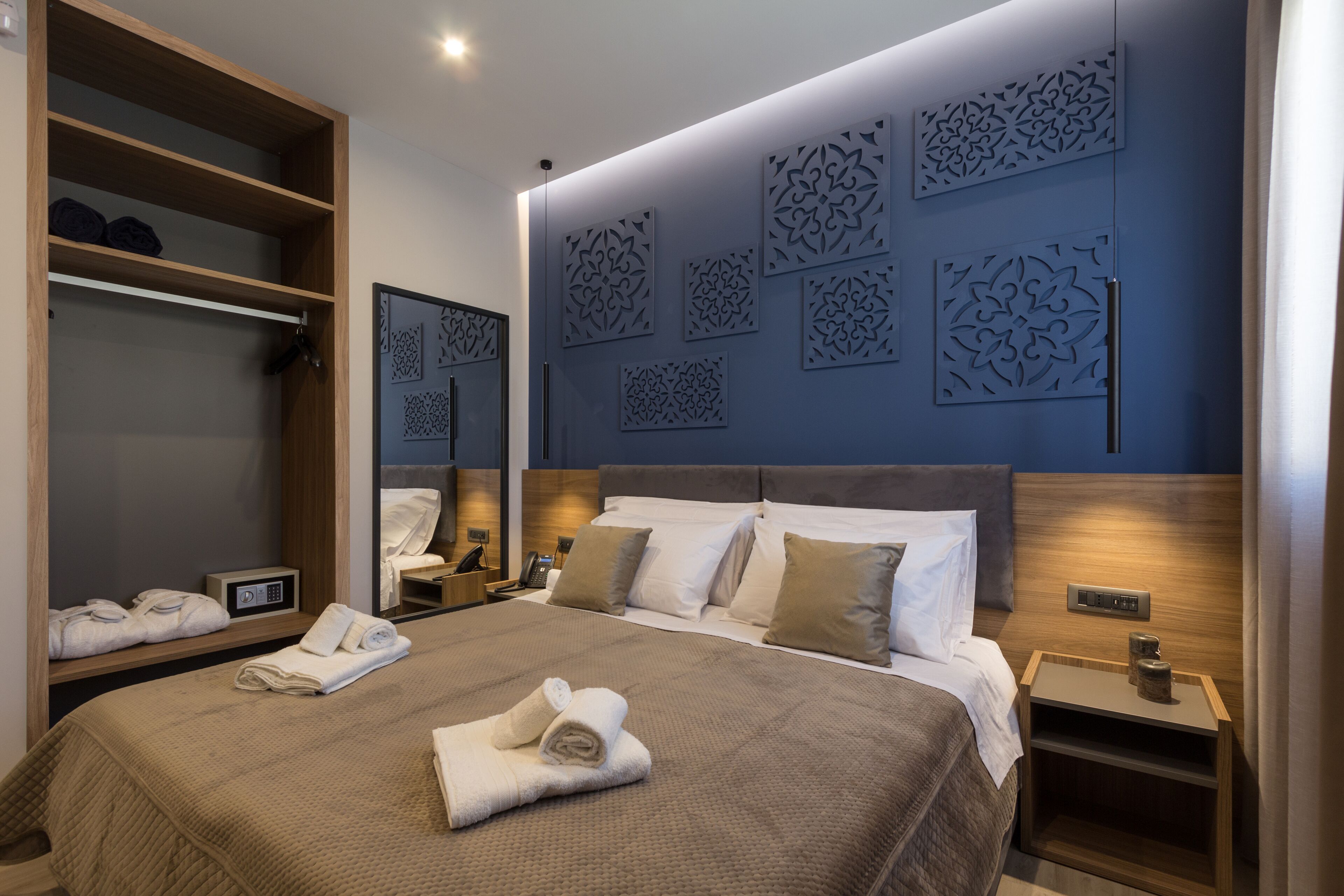 A neatly made bed with a brown quilt, a wooden wardrobe, and decorative wall panels.