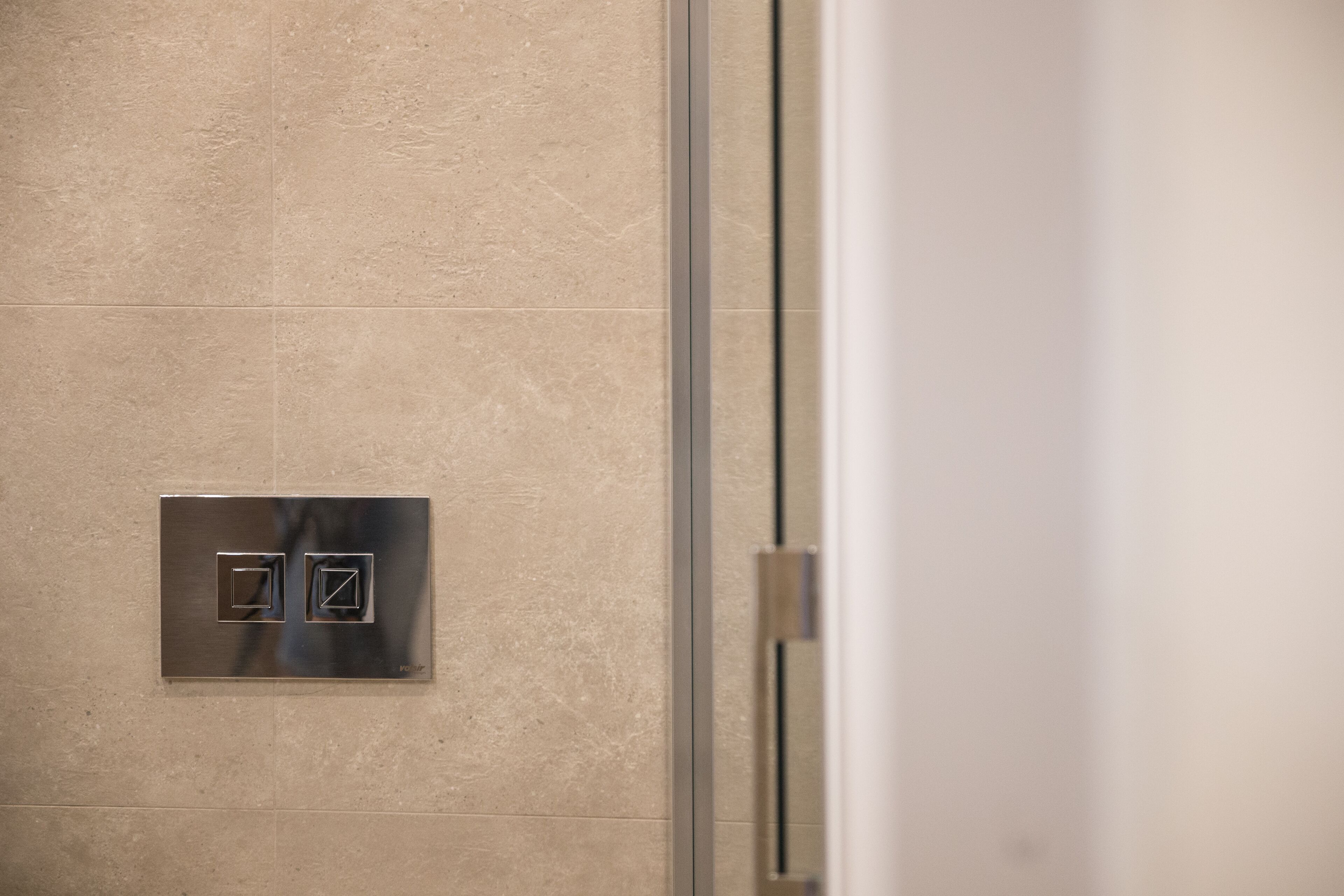 A bathroom with a metallic switch panel on the wall and a glass shower door.