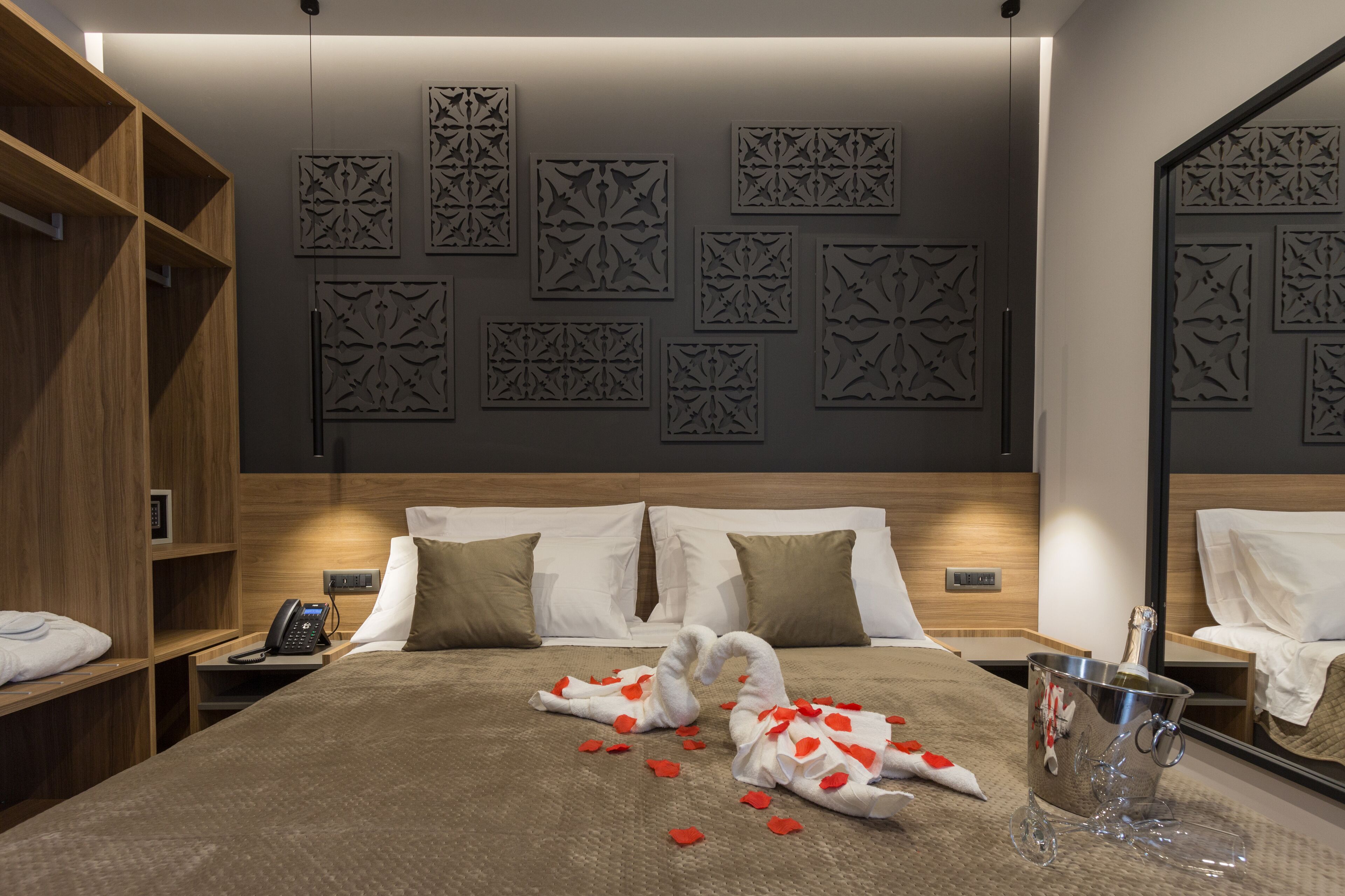 Habitación de hotel con una cama grande, una mesita de noche con teléfono, un minibar y paneles decorativos en la pared.