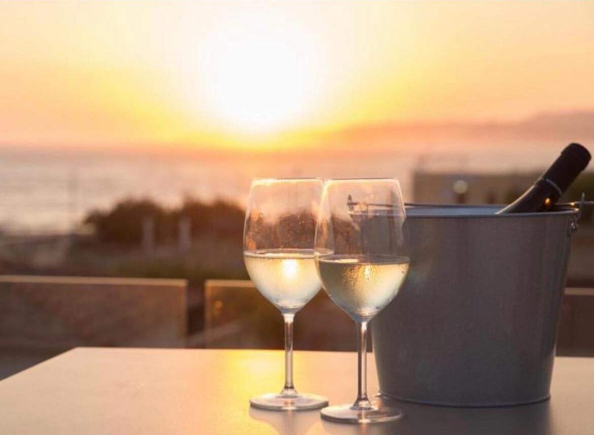 Two glasses of white wine on a table with a bottle of champagne, set against a sunset view.