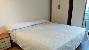 A neatly made bed with white linens, a wooden nightstand with drawers, and a wardrobe with two doors. - Ap. Annivè – Relaxation and comfort just steps from the heart of Levico Terme (Levico Terme)