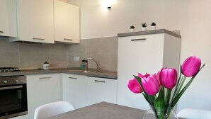 A modern kitchen with white cabinets, a gas stove, a sink, and a vase with pink tulips on the countertop. - Ap. Annivè – Relaxation and comfort just steps from the heart of Levico Terme (Levico Terme)