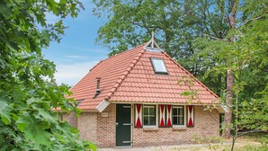 Une petite maison en briques avec un toit recouvert de tuiles rouges, une cheminée et une fenêtre surmontée d’un fronton triangulaire.