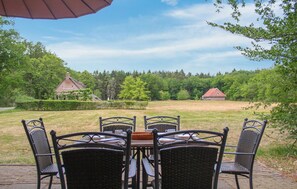Une terrasse avec une table et des chaises, donnant sur un espace verdoyant avec des arbres et un bâtiment en arrière-plan.