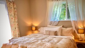 A bedroom with a bed, two bedside lamps, a window with sheer curtains, and a floral-patterned curtain on the left. - Ruby`s House ~ Downtown Durango (Durango)