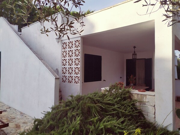 A white building with a covered outdoor area, a staircase, and a decorative wall panel.