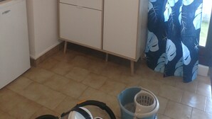 Ett litet, praktiskt kök med mikrovågsugn, kaffebryggare och brödrost. I förgrunden syns ett litet kylskåp, en blå hink och en cykel.