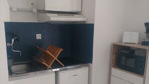 Ett kompakt kök med en diskho, ett litet kylskåp, en mikrovågsugn och ett skåp.