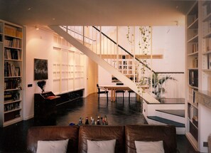 Uma sala de estar moderna com escada, estantes, área de jantar e um sofá.
