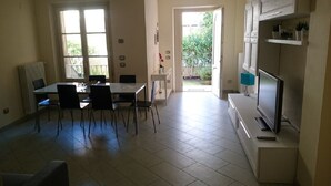 Un comedor con mesa y sillas, televisor y cocina con armarios y refrigerador.