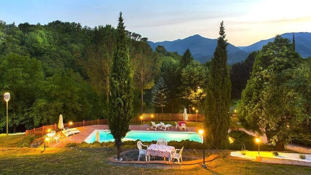 Un espace piscine doté de chaises longues et d’une table, entouré d’arbres et avec une chaîne de montagnes en toile de fond.