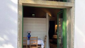 Un petit espace extérieur clos, aménagé avec une table et des chaises, un vase bleu et une fenêtre encadrée de vert.