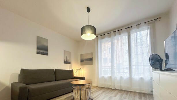 Een moderne woonkamer met een grijze bank, een ronde houten salontafel en een hanglamp.