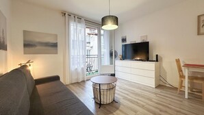 Een moderne woonkamer met een bank, een ronde salontafel, een televisie en een eethoek met een stoel en tafel.