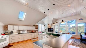 A modern kitchen with white cabinetry, a large island, and pendant lighting. - Cozy Cottage, Old Baldy Lighthouse Views, BHI (Bald Head Island)