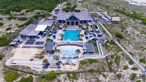 An aerial view of a resort with a central pool, multiple guest rooms, and a beach area. - Cozy Cottage, Old Baldy Lighthouse Views, BHI (Bald Head Island)
