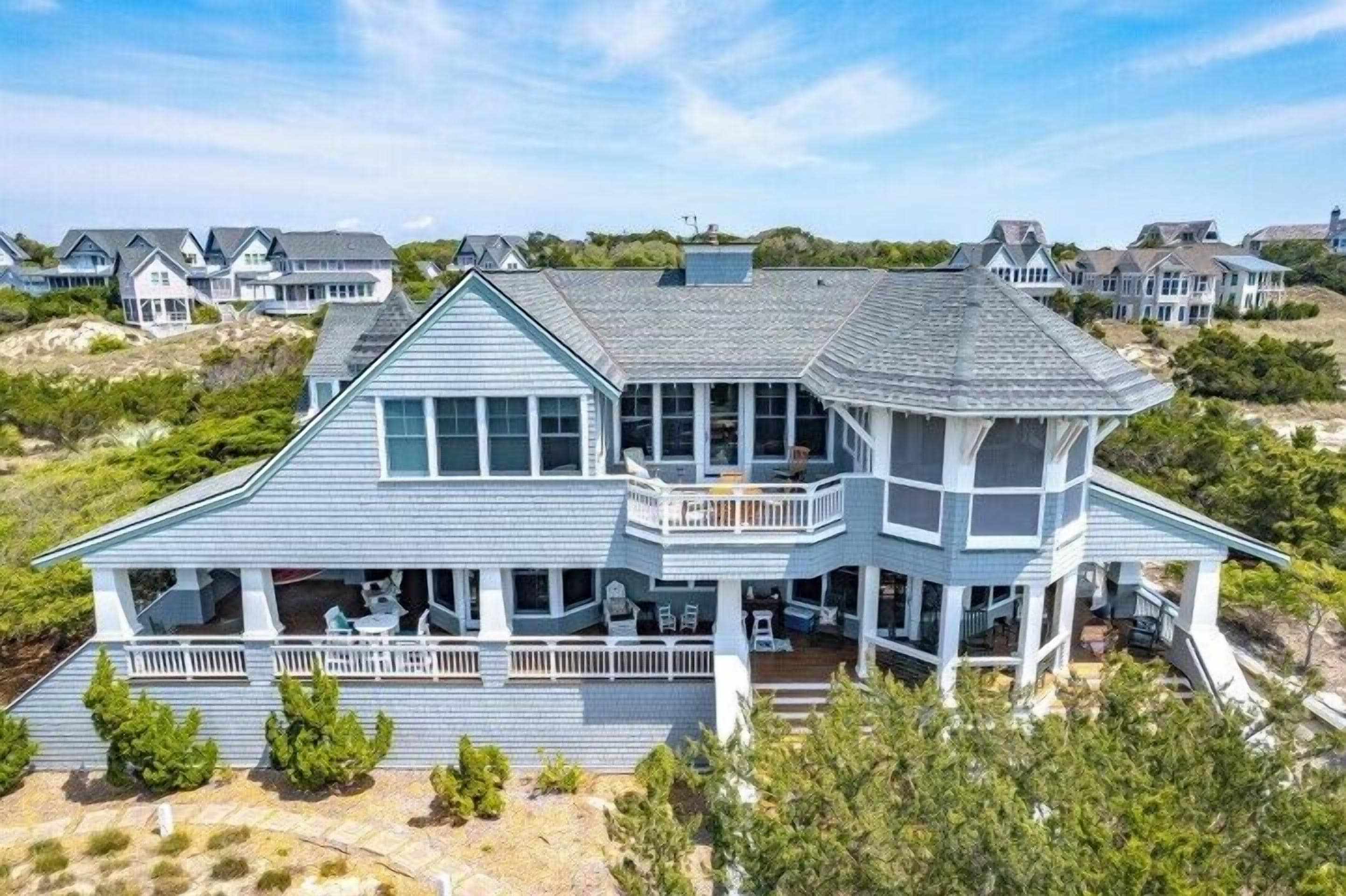 Ein großes, mehrstöckiges Strandhaus mit umlaufendem Balkon, zahlreichen Fenstern und einer überdachten Veranda.