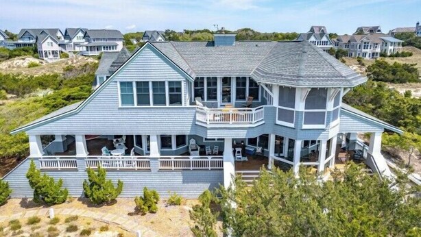 Ein großes, mehrstöckiges Strandhaus mit umlaufendem Balkon, zahlreichen Fenstern und einer überdachten Veranda.
