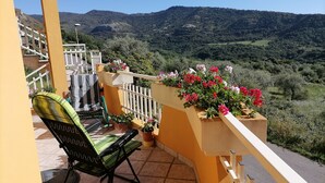 Ein Balkon mit einem Stuhl und Topfpflanzen, mit Blick auf eine gebirgige Landschaft.