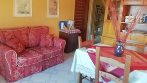 Ein Wohnzimmer mit einem blumigen Sofa, einem kleinen Tisch mit einer Vase und einem Bücherregal.