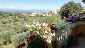 Ein Balkon mit Blick auf ein Küstendorf und ein Garten mit blühenden Pflanzen.