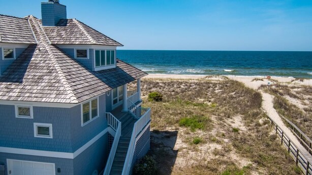 A two-story house with a beach view, a covered porch, and a sandy beach area. - Spacious Oceanfront home near golf and pool, BHI (Bald Head Island)